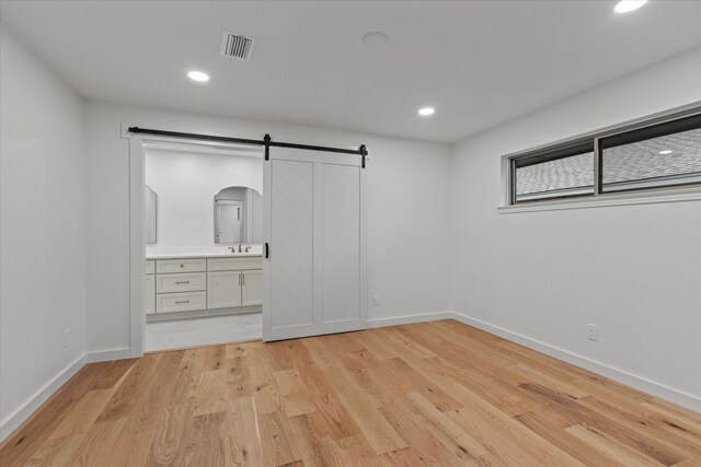unfurnished bedroom featuring a barn door, light wood-type flooring, baseboards, and recessed lighting