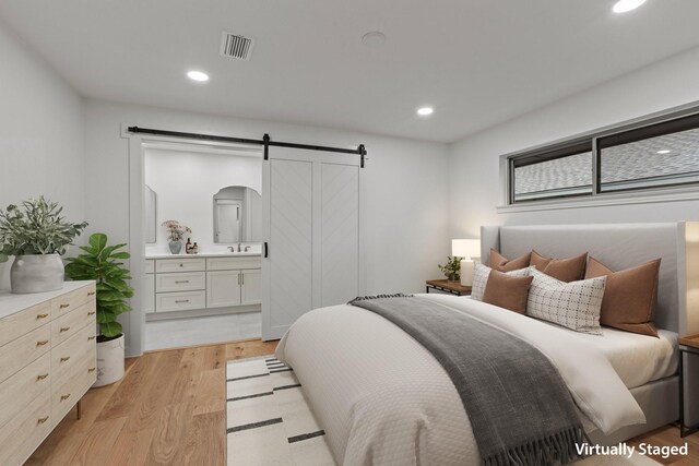 bedroom with a barn door, light wood-type flooring, recessed lighting, a sink, and ensuite bath