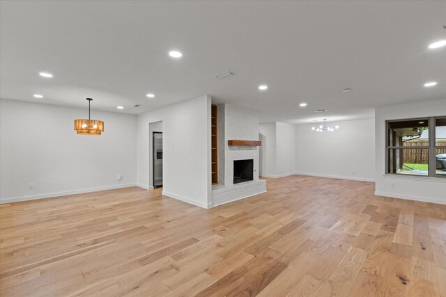 unfurnished living room with a chandelier, recessed lighting, a brick fireplace, light wood finished floors, and baseboards