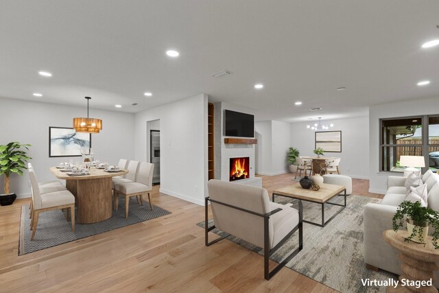 living area featuring a chandelier, light wood finished floors, a lit fireplace, recessed lighting, and baseboards