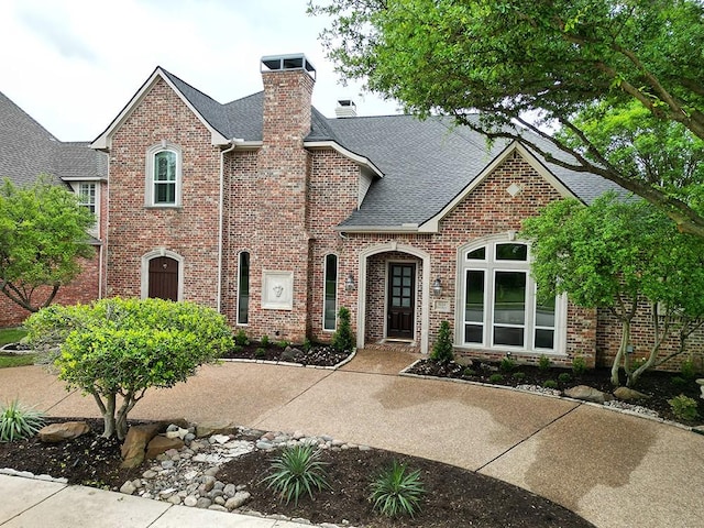 view of front of house with brick siding, a shingled roof, and a chimney