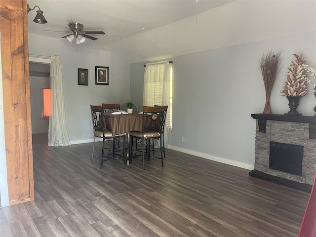 dining area featuring wood finished floors, a fireplace, baseboards, a ceiling fan, and vaulted ceiling