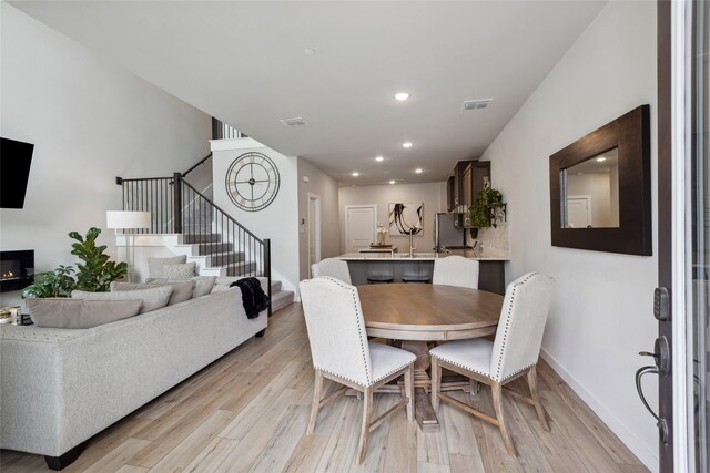 dining area with visible vents, light wood finished floors, baseboards, and stairway