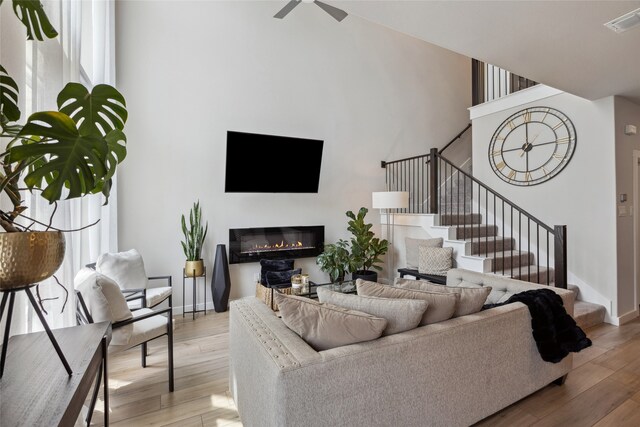 living room featuring visible vents, stairs, a glass covered fireplace, light wood-style floors, and a ceiling fan