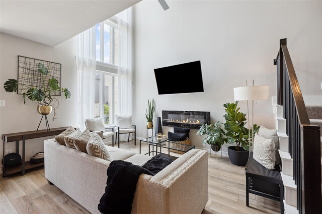 living room featuring a healthy amount of sunlight, a glass covered fireplace, light wood-type flooring, and a towering ceiling