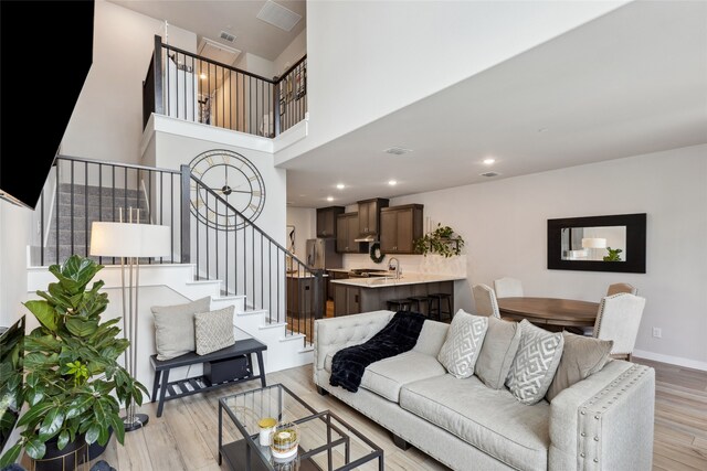 living area featuring visible vents, stairs, a towering ceiling, recessed lighting, and light wood finished floors