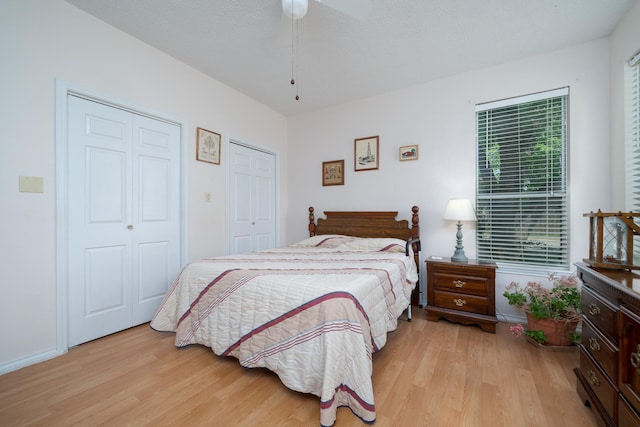 bedroom featuring baseboards, light wood finished floors, ceiling fan, and two closets