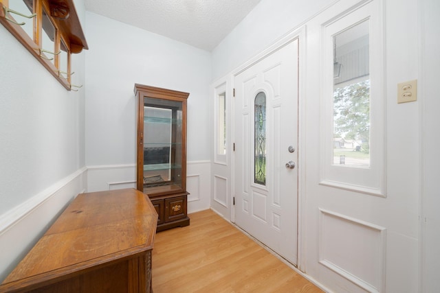 entryway featuring light wood-style floors, a textured ceiling, and wainscoting