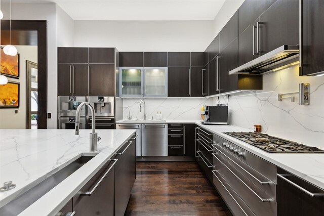 kitchen featuring appliances with stainless steel finishes, light stone counters, a sink, backsplash, and under cabinet range hood