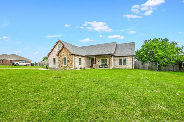 view of front of property featuring stone siding, fence, roof with shingles, and a front lawn