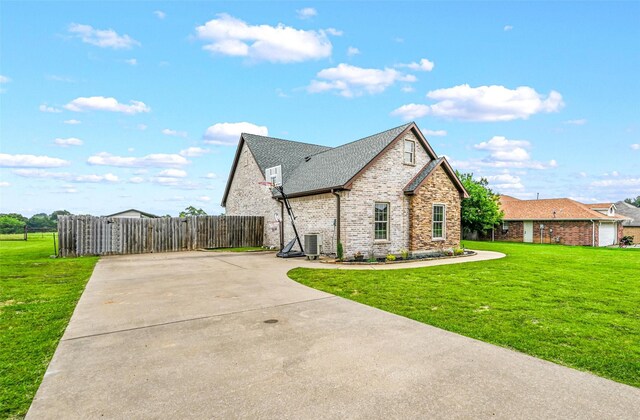 view of home's exterior featuring fence, cooling unit, roof with shingles, brick siding, and a yard