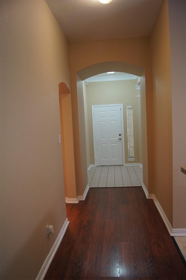 hallway featuring arched walkways, baseboards, and wood finished floors