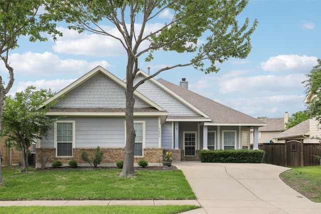craftsman-style home featuring fence, roof with shingles, a front lawn, brick siding, and a chimney