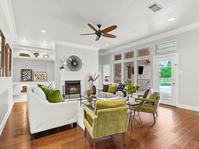 living area featuring a ceiling fan, visible vents, crown molding, baseboards, and a glass covered fireplace