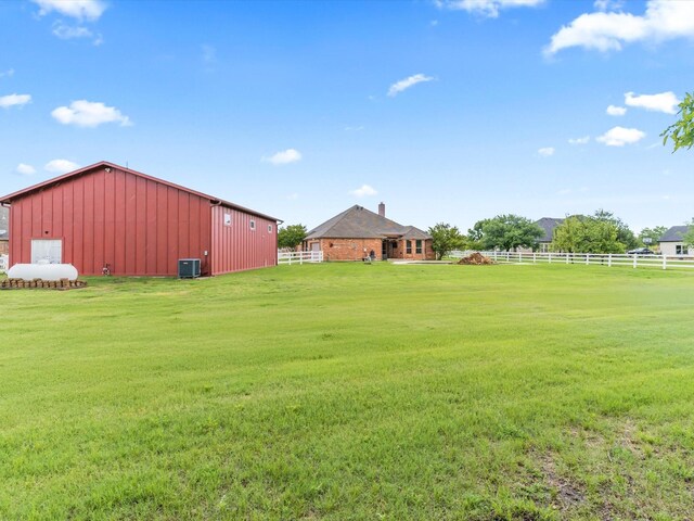 view of yard with an outdoor structure, fence, central AC unit, a rural view, and an outbuilding