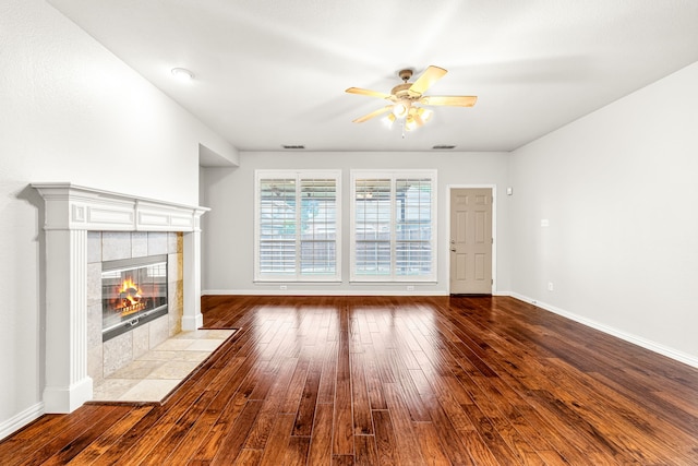unfurnished living room with ceiling fan, dark wood finished floors, a tiled fireplace, and baseboards