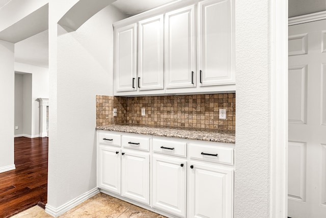 kitchen with decorative backsplash, baseboards, white cabinetry, light stone counters, and light wood-style flooring