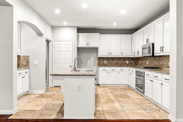 kitchen with a center island with sink, light stone counters, a sink, appliances with stainless steel finishes, and backsplash