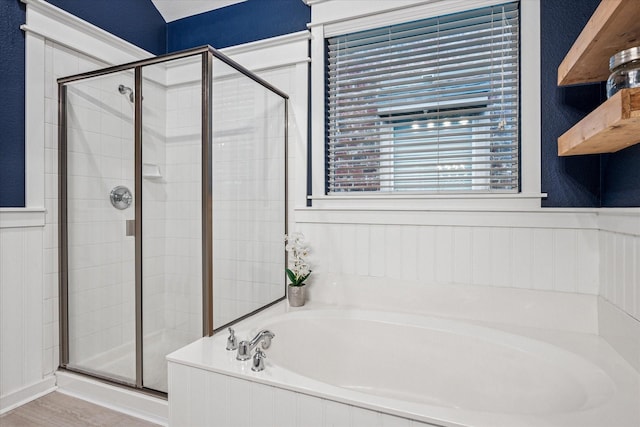 bathroom with a bath, a decorative wall, a stall shower, and a wainscoted wall