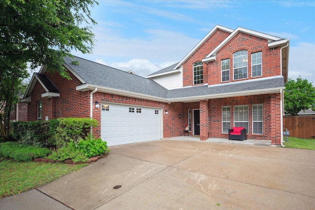 traditional-style house featuring a garage, fence, roof with shingles, brick siding, and driveway