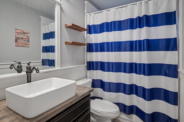 bathroom featuring toilet, a textured wall, a shower with shower curtain, and vanity