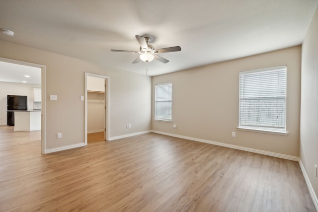 unfurnished bedroom featuring ceiling fan, light wood finished floors, baseboards, a spacious closet, and a closet