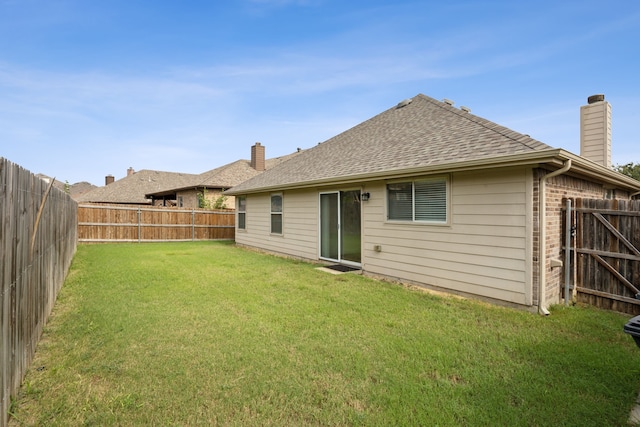 back of property featuring a fenced backyard, roof with shingles, a chimney, brick siding, and a yard