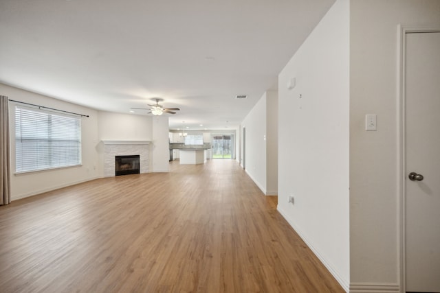 unfurnished living room featuring ceiling fan, visible vents, a fireplace, light wood-type flooring, and baseboards