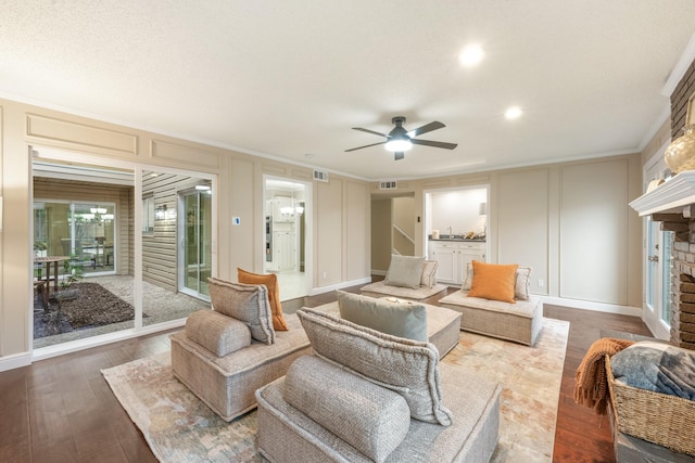 living room with visible vents, ornamental molding, a brick fireplace, a decorative wall, and a ceiling fan