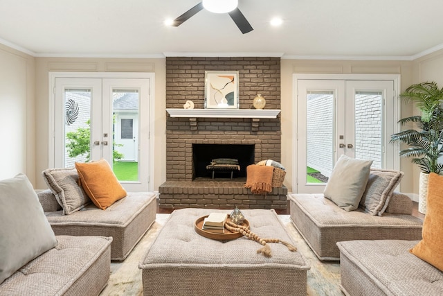 living area with a brick fireplace, a ceiling fan, ornamental molding, and french doors