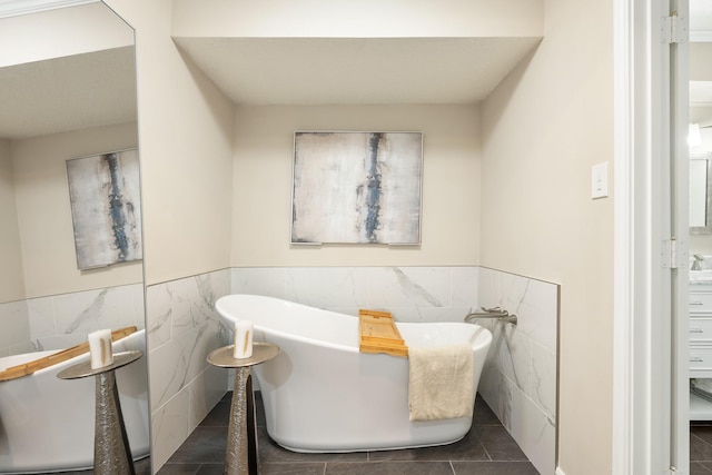 bathroom with a wainscoted wall, tile patterned flooring, a soaking tub, and tile walls