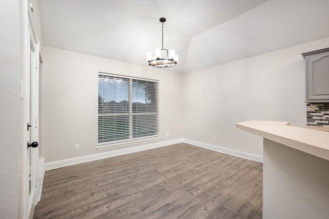 unfurnished dining area featuring an inviting chandelier, baseboards, vaulted ceiling, and dark wood finished floors