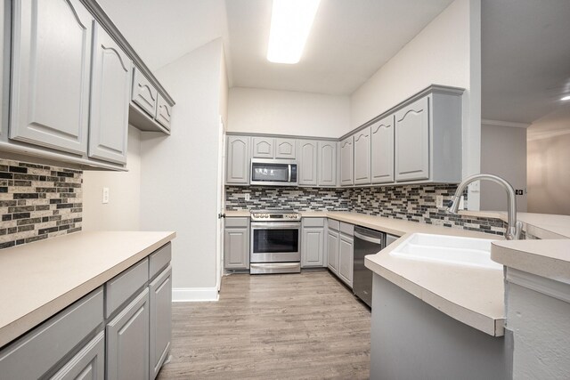 kitchen with a sink, decorative backsplash, gray cabinetry, and stainless steel appliances