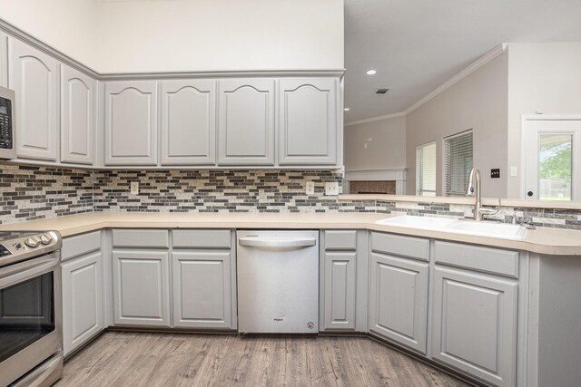 kitchen featuring a sink, light wood-style flooring, stainless steel appliances, backsplash, and ornamental molding