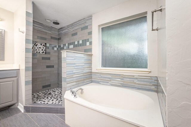 bathroom featuring tile patterned flooring, a tile shower, a garden tub, and vanity