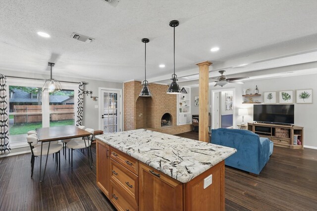kitchen with brown cabinetry, a ceiling fan, dark wood-style flooring, visible vents, and a fireplace