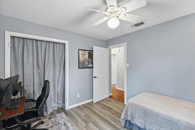 bedroom featuring ceiling fan, a textured ceiling, baseboards, wood finished floors, and visible vents