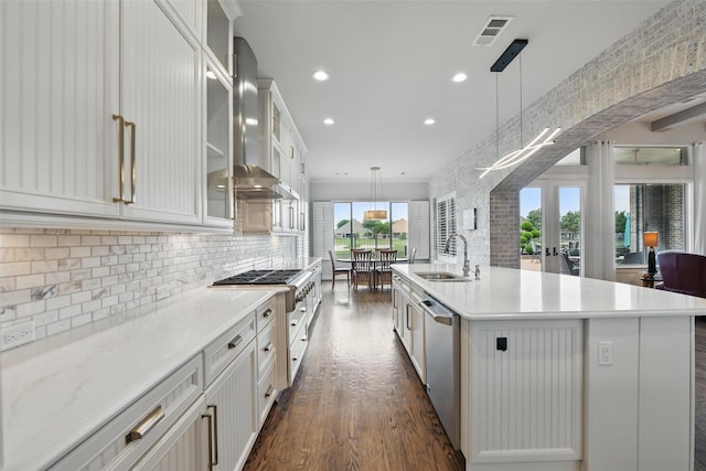 kitchen with backsplash, visible vents, a center island with sink, a sink, and dark wood-type flooring
