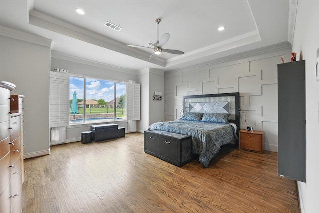 bedroom featuring recessed lighting, wood finished floors, a tray ceiling, visible vents, and ornamental molding