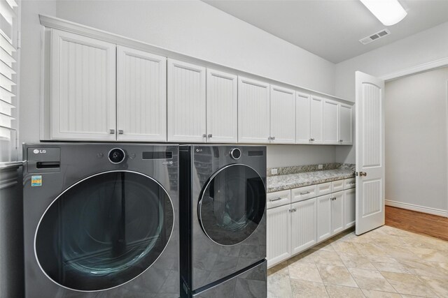 washroom with visible vents, cabinet space, baseboards, and washer and dryer
