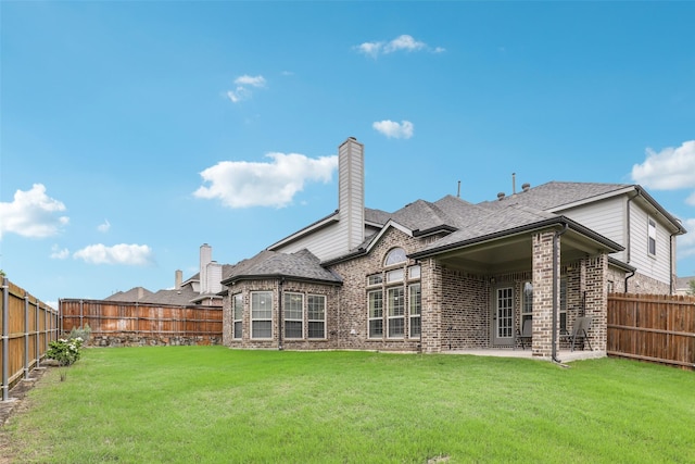 back of property with brick siding, a fenced backyard, a lawn, and a chimney