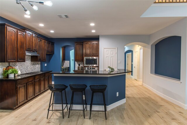 3501 Washington Dr, Frisco, TX 75034 - kitchen with stainless steel microwave, arched walkways, under cabinet range hood, light wood-type flooring, and a kitchen bar