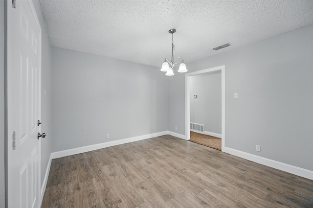 empty room featuring visible vents, a textured ceiling, wood finished floors, and a notable chandelier