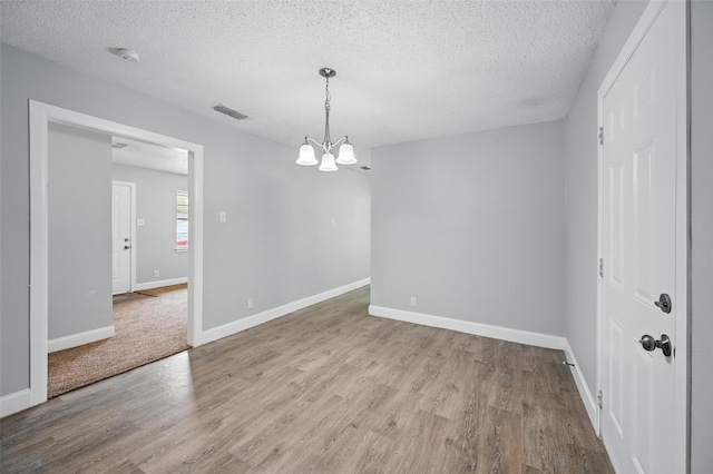 unfurnished room with visible vents, wood finished floors, baseboards, a textured ceiling, and a notable chandelier