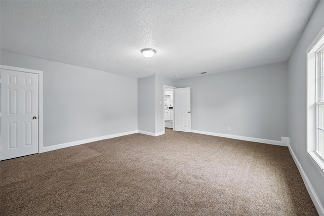 empty room with carpet flooring, a textured ceiling, and baseboards
