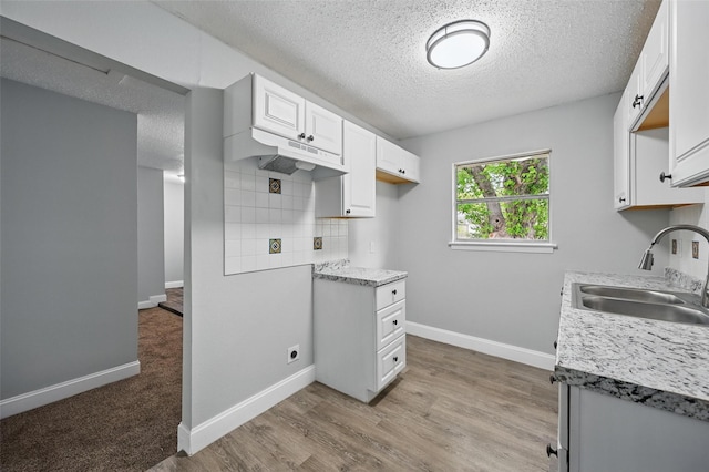 kitchen featuring a sink, a textured ceiling, under cabinet range hood, and light countertops