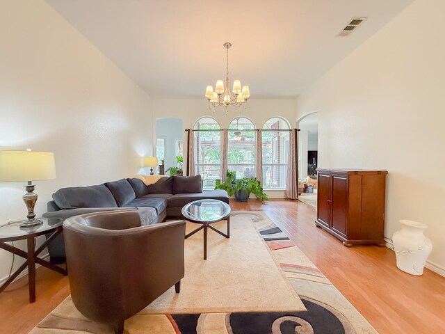 living room featuring visible vents, arched walkways, light wood-style flooring, and a notable chandelier