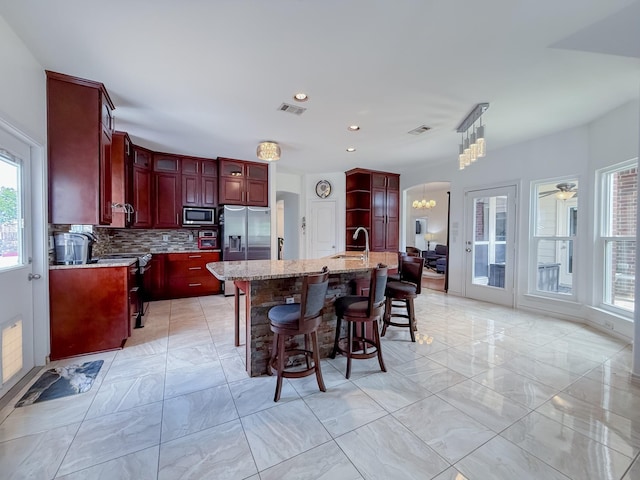 200 Meadowside Dr, Mansfield, TX 76063 - kitchen with stainless steel appliances, a ceiling fan, a stone fireplace, backsplash, and light stone counters