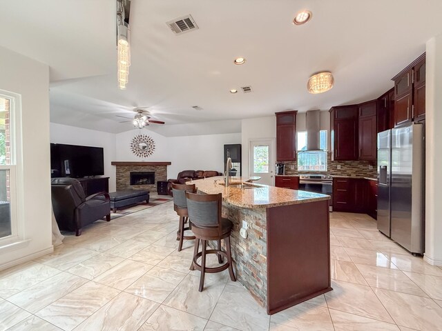 kitchen featuring a fireplace, wall chimney exhaust hood, stainless steel appliances, decorative backsplash, and visible vents