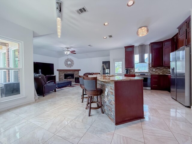 200 Meadowside Dr, Mansfield, TX 76063 - kitchen with appliances with stainless steel finishes, a fireplace, wall chimney exhaust hood, decorative backsplash, and a ceiling fan